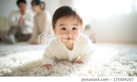 一個嬰兒正朝他們爬過來,父母在後面看著。 一個嬰兒正朝他們爬過來,父母在後面看著。 135884267