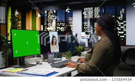 Green screen next to black female expert checking social media content, video editing with dual monitors in office. Woman enhancing visibility, engagement and reach for branding. Camera A. 135884434