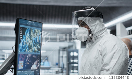 Scientist in hazmat suit checking DNA molecules of infected patient in a bioscience lab, analyzing pathology and virology data, testing immunology theories and developing vaccines. Camera B. Scientist in hazmat suit checking DNA molecules of infected patient in a bioscience lab, analyzing pathology and virology data, testing immunology theories and developing vaccines. Camera B. 135884448