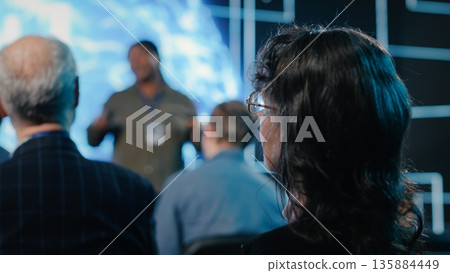 Senior female in the audience listening to AI sales pitch featuring neural networks, AI brain machine learning. Entrepreneur speaker explains funding and investment deal opportunities. Senior female in the audience listening to AI sales pitch featuring neural networks, AI brain machine learning. Entrepreneur speaker explains funding and investment deal opportunities. 135884449
