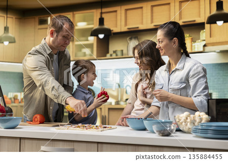 Family of four preparing a delicious homemade pizza together, enjoying fun weekend activity in the kitchen. Parents guiding children through the recipe as they sprinkle ingredients. Family of four preparing a delicious homemade pizza together, enjoying fun weekend activity in the kitchen. Parents guiding children through the recipe as they sprinkle ingredients. 135884455