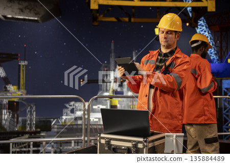 Industrial skilled worker on offshore drilling rig evaluates data for petroleum extraction, technology used to manage efficient fossil fuels and gas production from the ocean environment. Industrial skilled worker on offshore drilling rig evaluates data for petroleum extraction, technology used to manage efficient fossil fuels and gas production from the ocean environment. 135884489