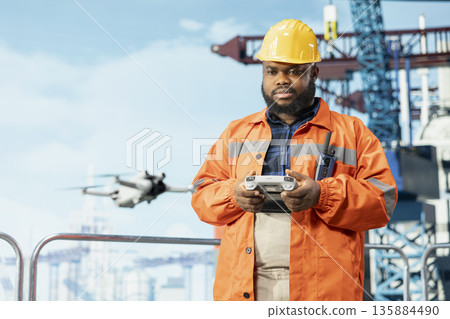 Drilling rig technician using drone to access areas that pose environmental risks to humans from safe distance. Man on offshore platform deck uses remote control UAV to conduct aerial surveys 135884490