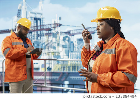Drilling rig team leader uses two way radio to establish communication with logistics personnel. Offshore platform expert speaks in walkie talkie providing audio clarity in noisy environment 135884494