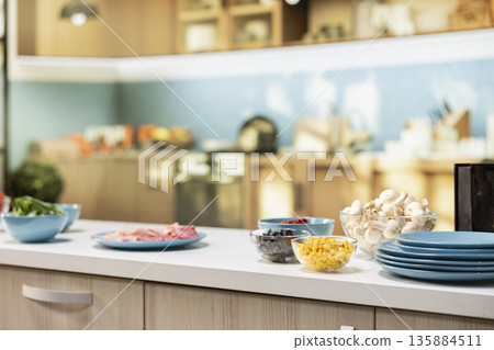 Modern kitchen setup with pizza ingredients on a countertop. Bowls of corn, olives, mushrooms and pepperoni placed on counter beside herbs and kitchenware, fun cooking activity. Modern kitchen setup with pizza ingredients on a countertop. Bowls of corn, olives, mushrooms and pepperoni placed on counter beside herbs and kitchenware, fun cooking activity. 135884511