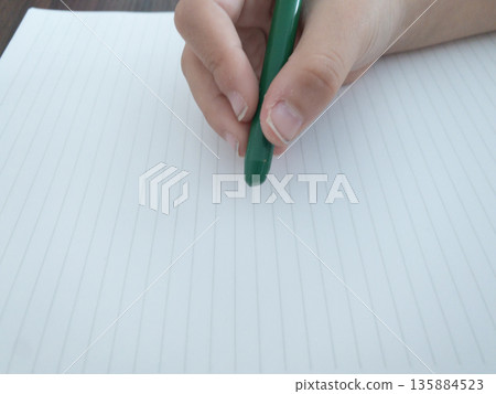 Child's hand holding a green pen over a notebook Child's hand holding a green pen over a notebook 135884523