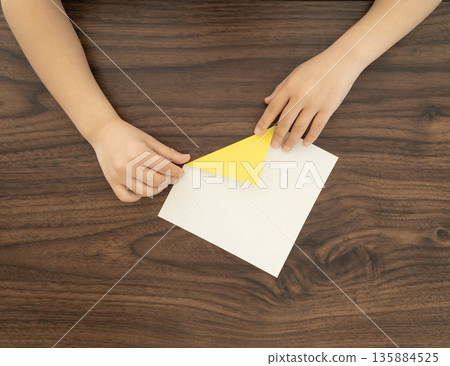 Child's hands folding white and yellow origami paper Child's hands folding white and yellow origami paper 135884525