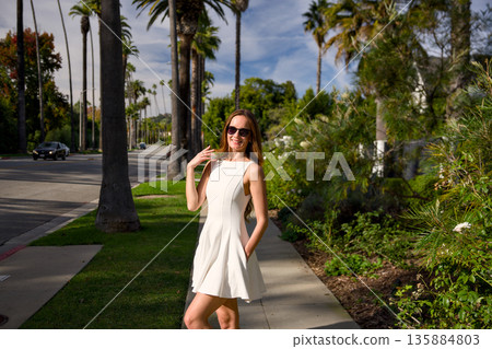 Young woman in white dress walking along palm tree lined street Young woman in white dress walking along palm tree lined street 135884803
