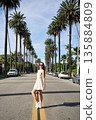 Woman in white dress standing on palm lined street on sunny day 135884809