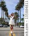 Young woman in white dress standing on palm tree lined street 135884811