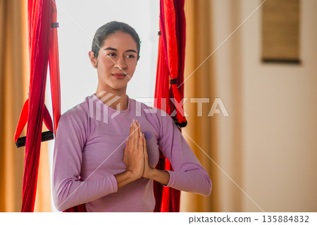 Young latin woman practicing aerial yoga meditation indoors Young latin woman practicing aerial yoga meditation indoors 135884832