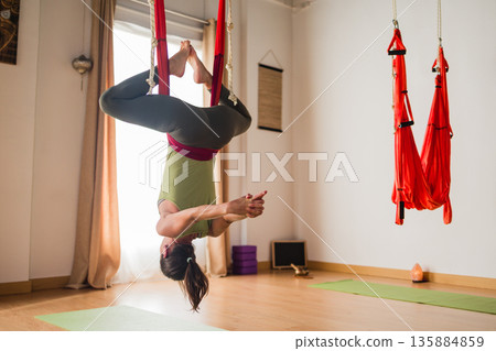 Woman practicing aerial yoga inversion in hammock 135884859