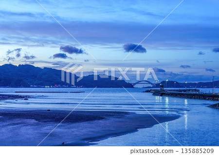A view of the calm coastline during blue hour and the Kushimoto Bridge in the distance A view of the calm coastline during blue hour and the Kushimoto Bridge in the distance 135885209