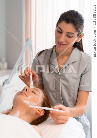 Happy beautician applying face mask to woman with Happy beautician applying face mask to woman with 135885215