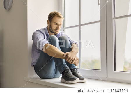 Sad man at window, coping with depression, loneliness, anxiety, and life stress 135885504