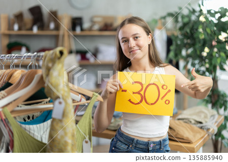 Teen girl holding discount sign in clothing store Teen girl holding discount sign in clothing store 135885940