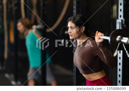 Latina woman with a barbell on her shoulders doing squats and lunges Latina woman with a barbell on her shoulders doing squats and lunges 135886099
