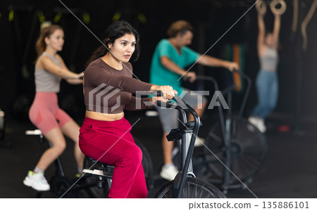 Sportive Latina girl doing air bike exercises in well-equipped gym 135886101