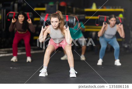 Determined young woman performing sandbag squats 135886116