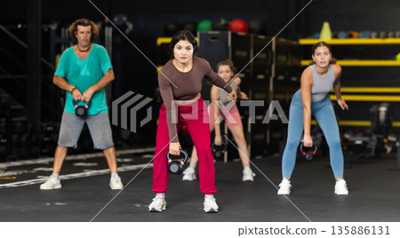 Sportive Latina girl lifting heavy kettlebell in sports hall 135886131