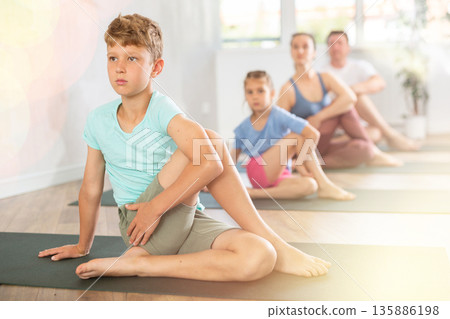 Diligent preteen boy practicing half lord of the fishes pose of yoga with his family 135886198