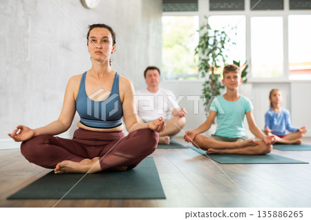 Adult woman with family practicing yoga in studio Adult woman with family practicing yoga in studio 135886265