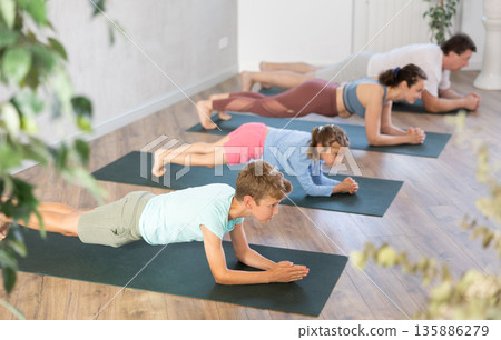 Diligent preteen boy practicing plank pose of yoga with his family 135886279