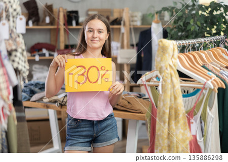 Teenage girl holding discount sign in clothing store Teenage girl holding discount sign in clothing store 135886298