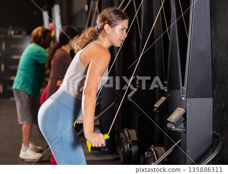 Determined young girl training her arms using cable exercise machine in gym 135886311