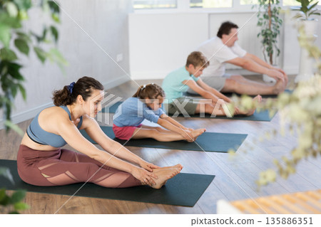 Preteen children with parents doing stretching and doing yoga on mats in gym Preteen children with parents doing stretching and doing yoga on mats in gym 135886351