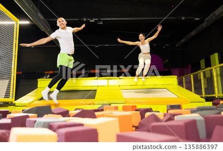 Happy athletes, man and girl, training to jump on trampolines at trampoline center Happy athletes, man and girl, training to jump on trampolines at trampoline center 135886397