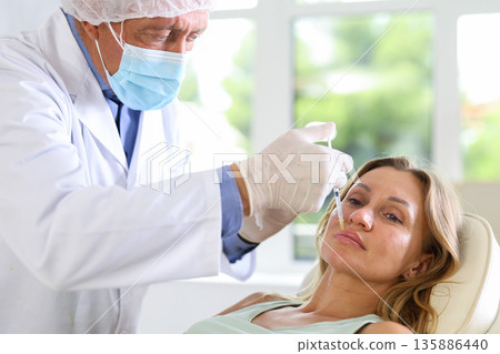 Male doctor gives injection and performs procedure of lip augmentation of female patient in clinic. Male doctor gives injection and performs procedure of lip augmentation of female patient in clinic. 135886440