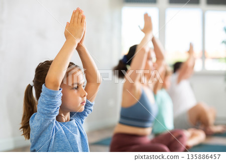 Pleasant little girl practicing lotus pose of yoga with her family 135886457