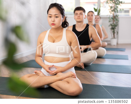 Sporty woman and man practise yoga, meditation in lotus position in fitness center 135886502