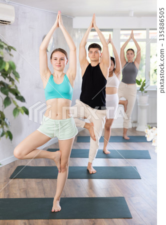 Slim young girl practicing tree pose of yoga on black mat 135886505