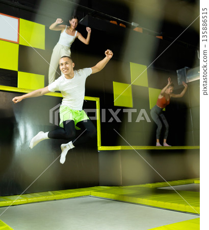 Emotional man jumping vertical and flying in trampoline sport center indoors 135886515