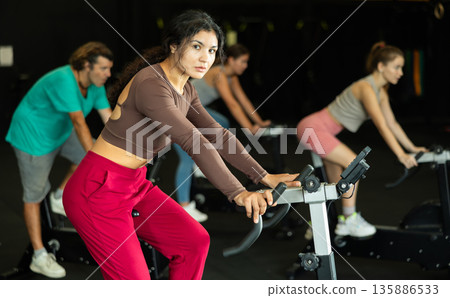 Latina woman exercising on an exercise bike in a crossfit gym Latina woman exercising on an exercise bike in a crossfit gym 135886533