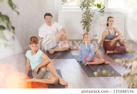 Diligent preteen boy practicing half lord of the fishes pose of yoga with his family 135886556
