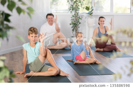 Diligent preteen boy practicing half lord of the fishes pose of yoga with his family 135886598