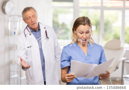 Female doctor reads paper documents report and shouts at elderly subordinate man 135886668
