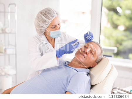 Woman cosmetologist makes injection in lips of man 135886684