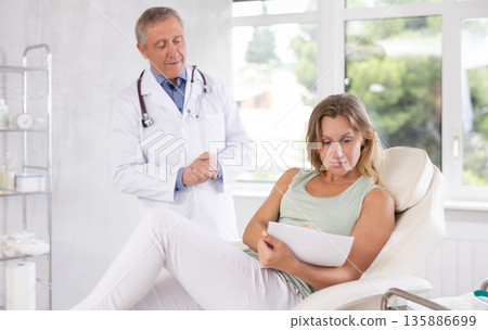Elderly man doctor giving agreement to patient for signing Elderly man doctor giving agreement to patient for signing 135886699