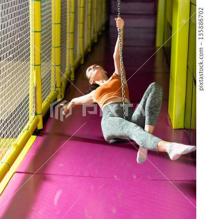 Woman enjoying riding zip line in colorful indoor amusement center 135886702