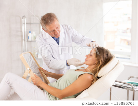 Middle-aged woman having consultation about face aesthetic while looking in the mirror 135886705