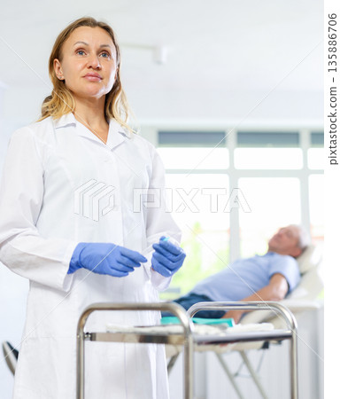Middle-aged female doctor preparing injection for woman patient 135886706