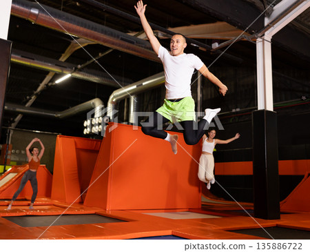 Fitness, fun, leisure and sport activity concept - happy man jumping on trampoline indoors Fitness, fun, leisure and sport activity concept - happy man jumping on trampoline indoors 135886722