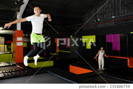 Cheerful young man jumping in modern indoor trampoline park Cheerful young man jumping in modern indoor trampoline park 135886739
