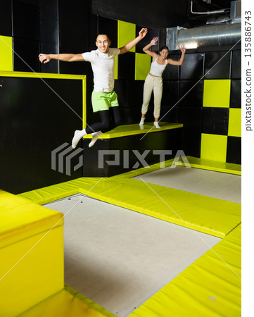 Joyful carefree young man leaping at trampoline park Joyful carefree young man leaping at trampoline park 135886743