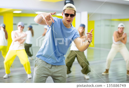 Expressive teenage boy dancer having group training in dance hall 135886749