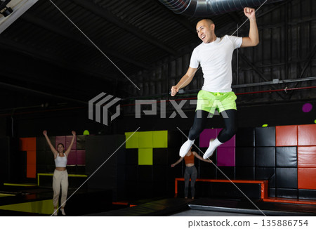 Cheerful young man jumping in modern indoor trampoline park Cheerful young man jumping in modern indoor trampoline park 135886754